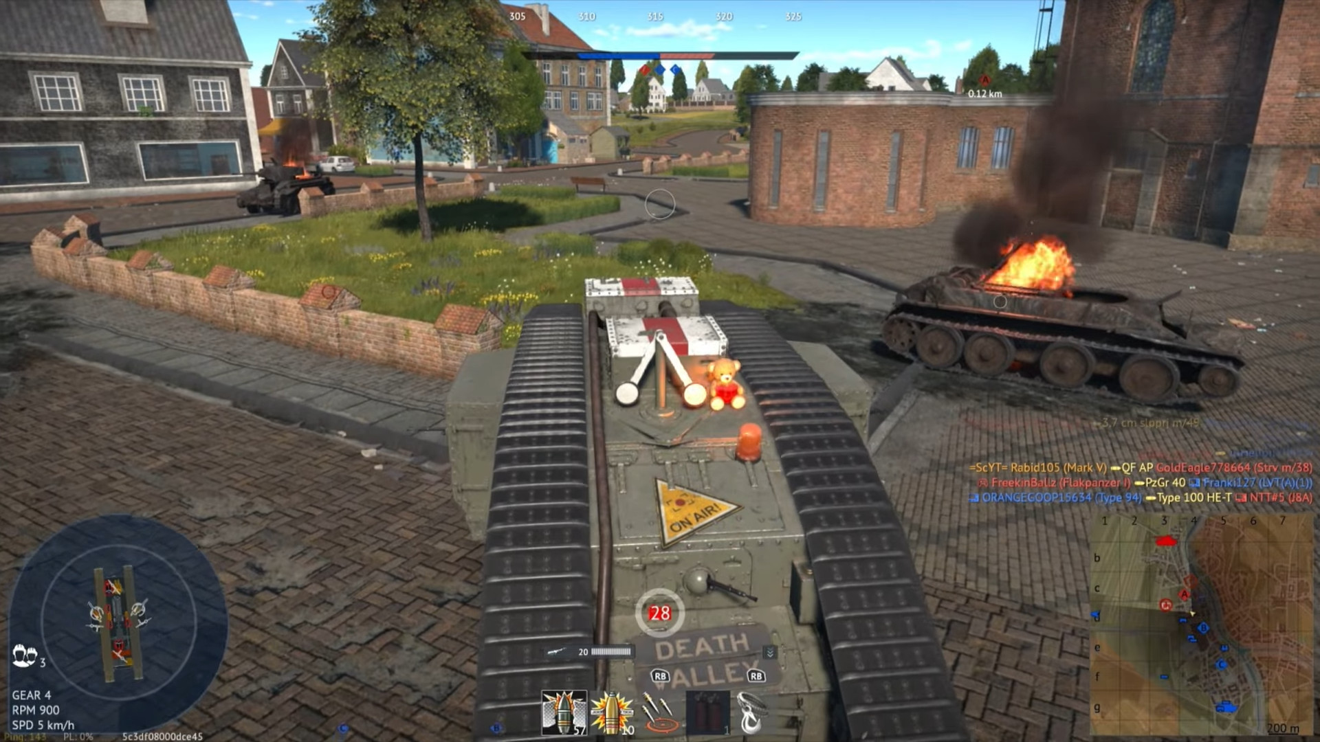 Third-person view from tank hull crossing cobblestone town square with burning enemy tank at right and destroyed tank at left